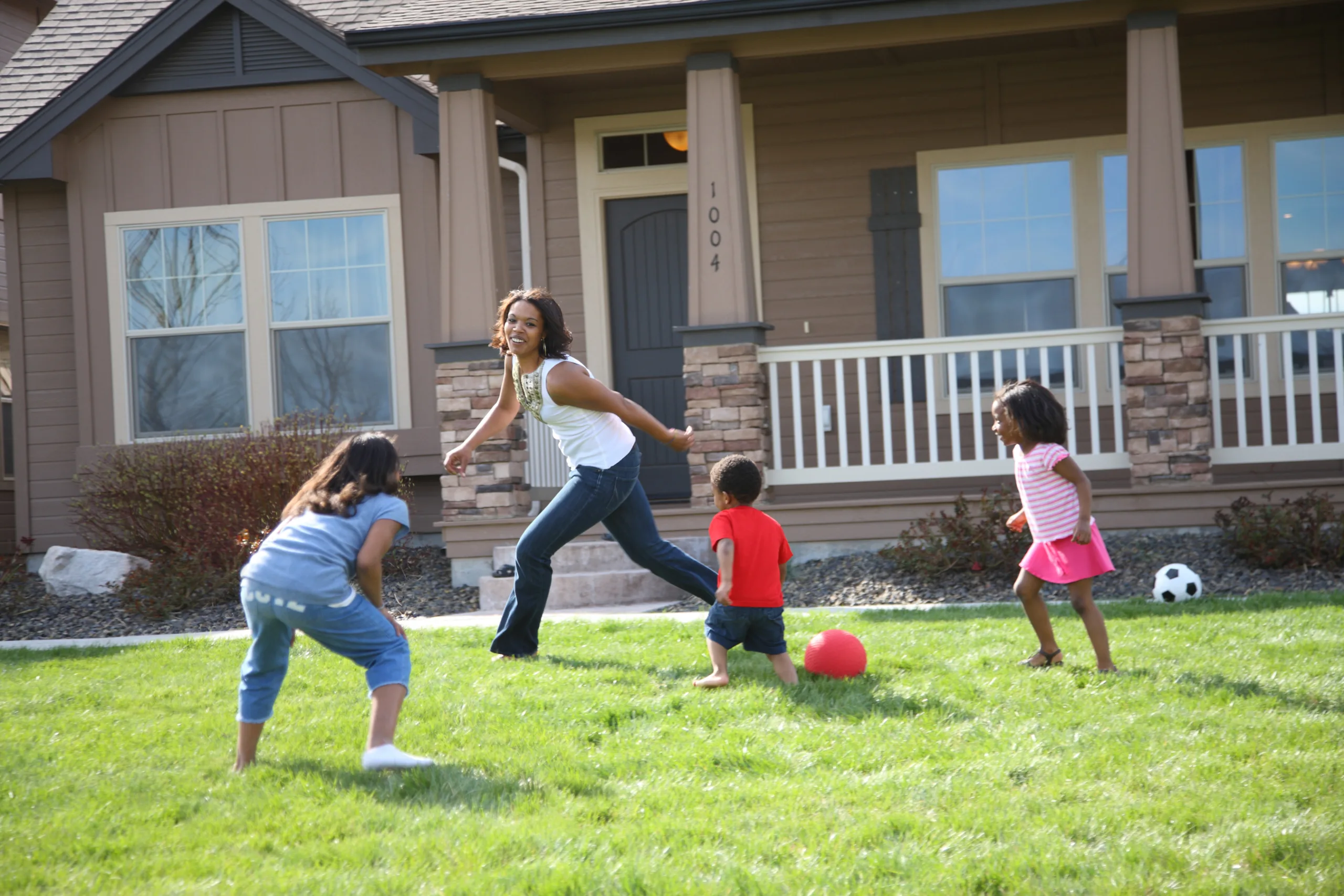 Woman playing soccer with three children in front of a residential house